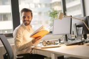 Čovek se smeje dok čita knjigu za kancelarijskim stolom